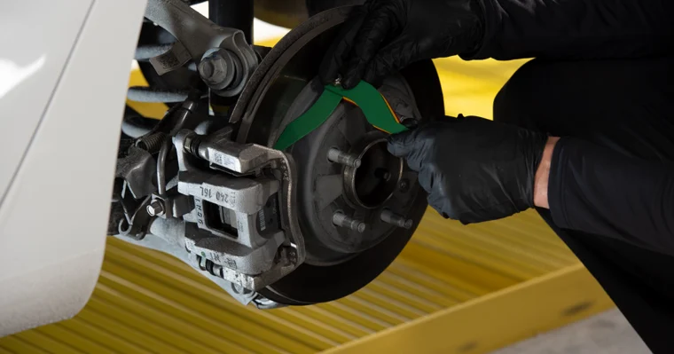 A person wearing black gloves checks or adjusts the brake components on a vehicle's exposed wheel assembly.