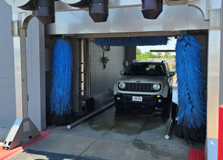 A white Jeep Renegade is inside an automatic car wash with blue spinning brushes on each side.