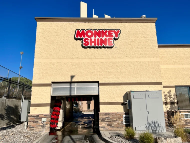Exterior view of a Monkey Shine car wash building with a drive-through entrance and bright signage on a sunny day.