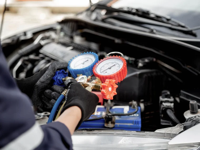 Close up of an auto mechanic using measuring gauge to check the refrigerant and filling car air conditioner for fix.
