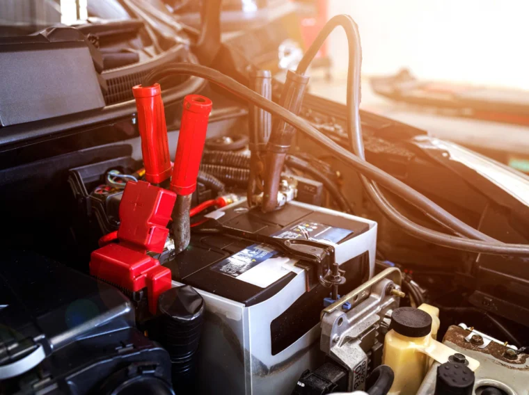 Close-up of a car battery with red and black jumper cables attached, illustrating starting services as the battery is being jump-started.