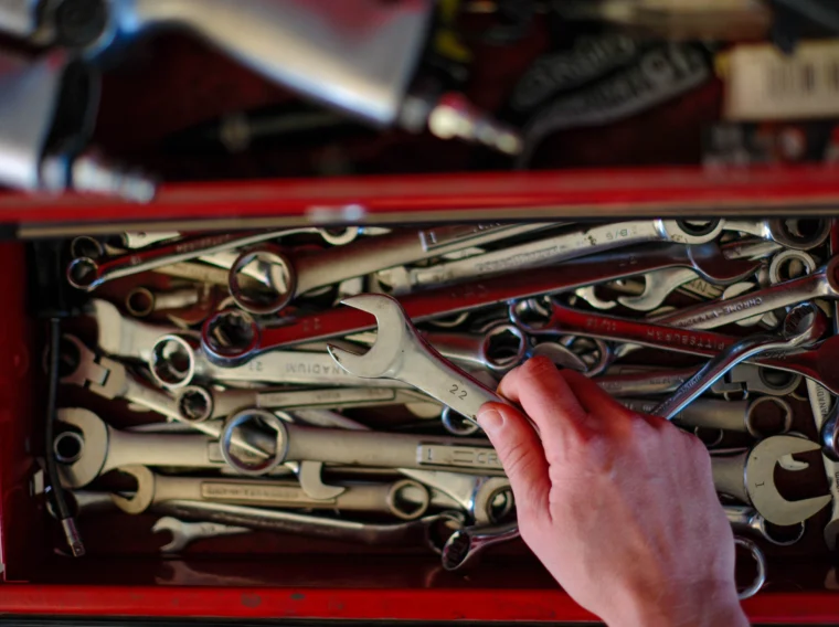 A hand picks up a wrench from a red toolbox drawer filled with various wrenches and hand tools, ready for tasks like clutch replacement.