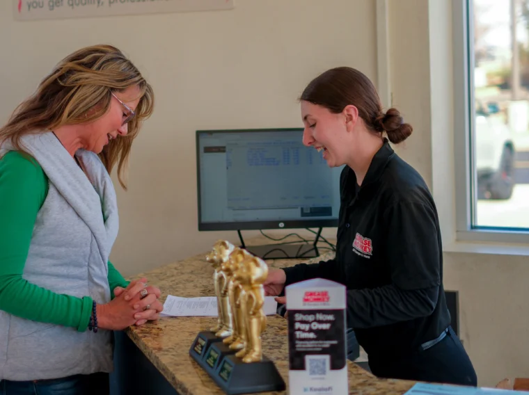 A customer and an employee interact at a Grease Monkey service counter, with trophies and informational materials highlighting their Engine Services displayed on the countertop.