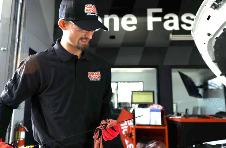 Grease Monkey mechanic holding a dipstick while checking engine oil.
