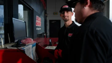Two Grease Monkey mechanics talking in front of a computer screen.