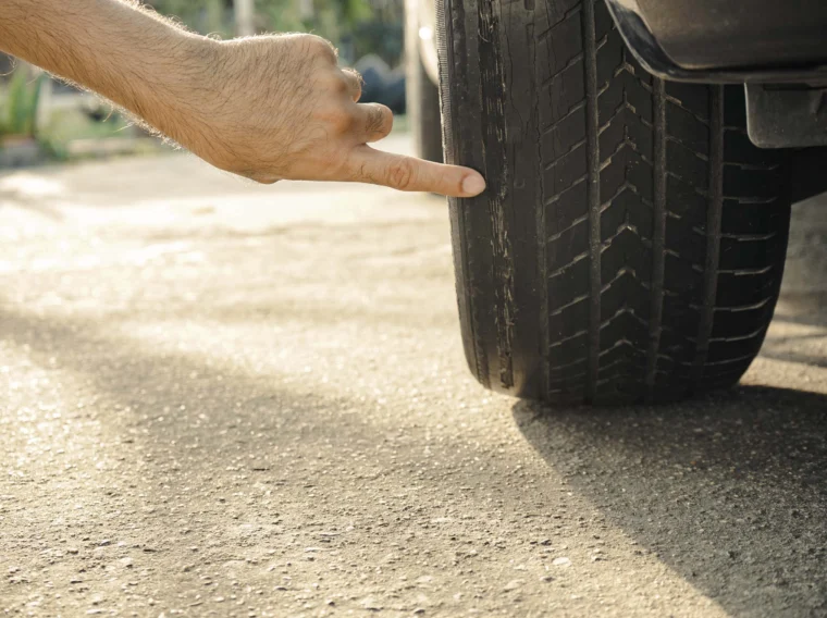 A finger pointing at a worn front car tire with bald tread.
