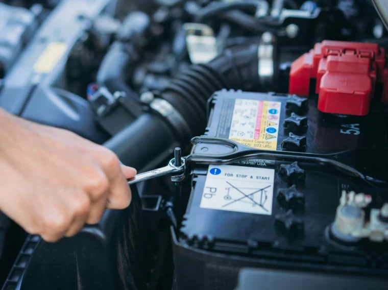 An auto technicians hand is tightening a bolt that is holding a car battery.
