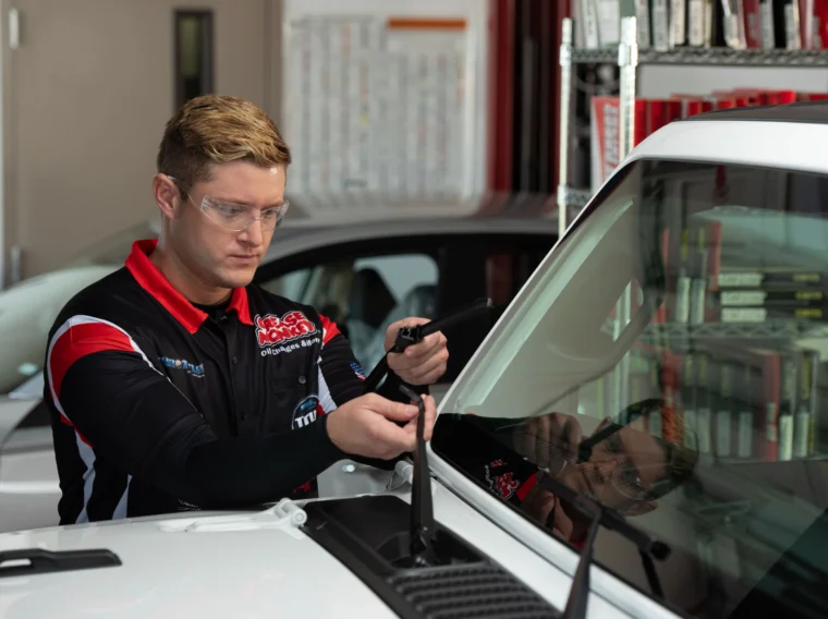 A Grease Monkey technician changing the wiper blades of a white vehicle.
