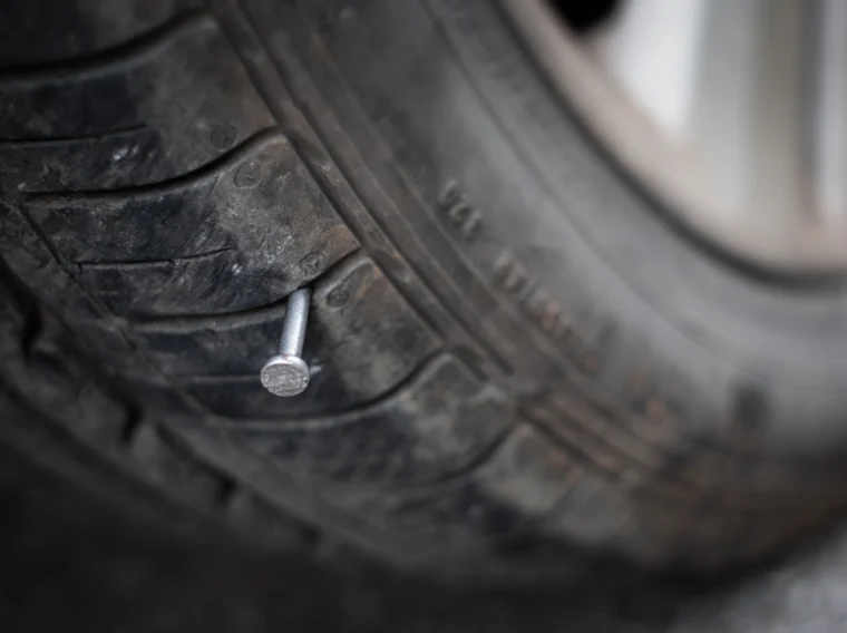 Close up of a metal nail sticking out of a tire.