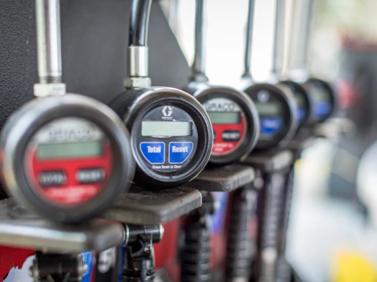 A row of digital meters with Total and Reset buttons, each attached to dispensing hoses, is mounted on a metal surface.