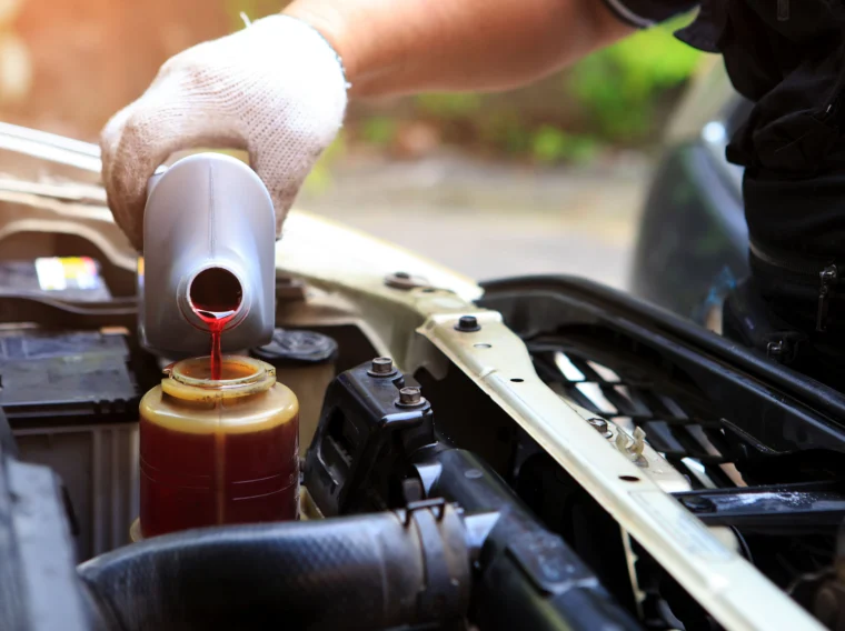 A hand filling a car's power steering fluid reservoir.