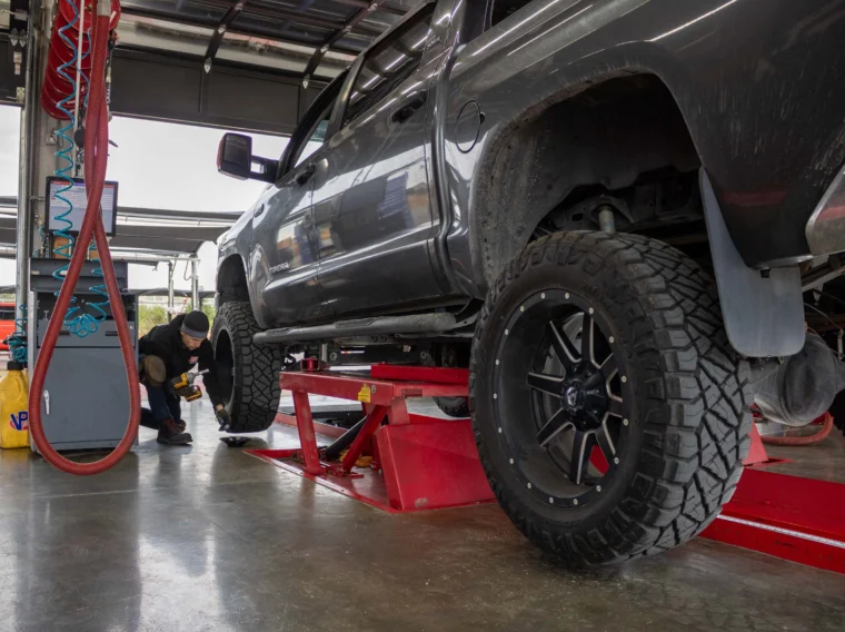 An auto technician rotating the tires of a pickup truck.