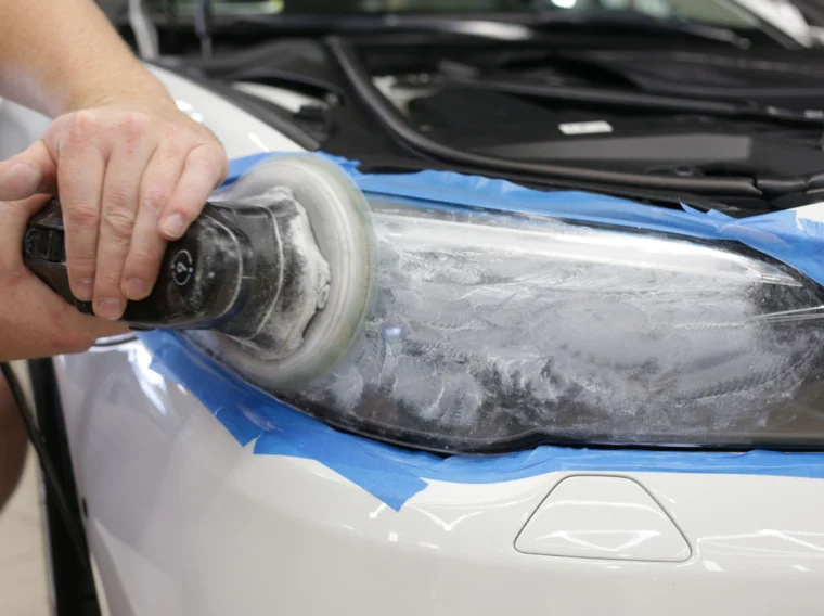 A hand holding a buffer tool and cleaning a vehicle's headlights.