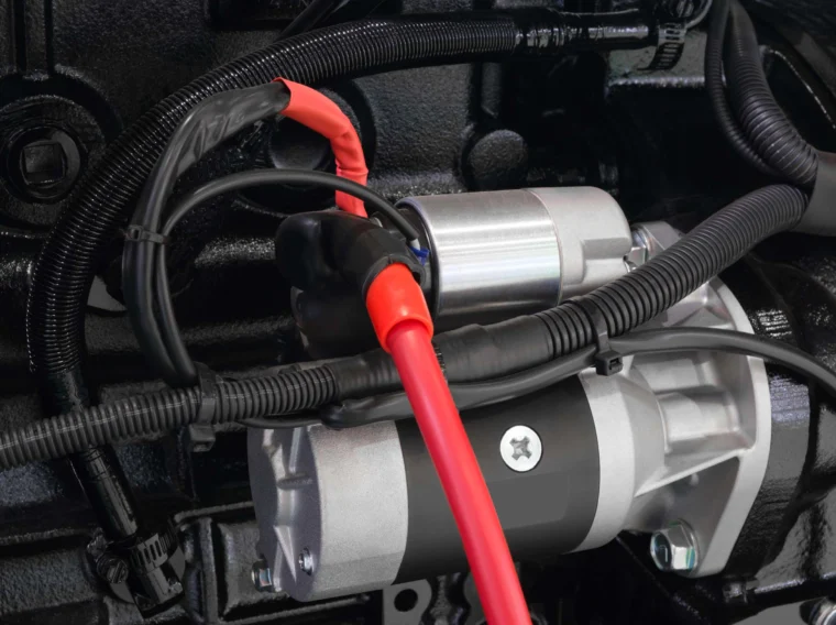 Close-up view of a car starter motor with attached red and black electrical cables and surrounding wiring, essential components for reliable starting services.