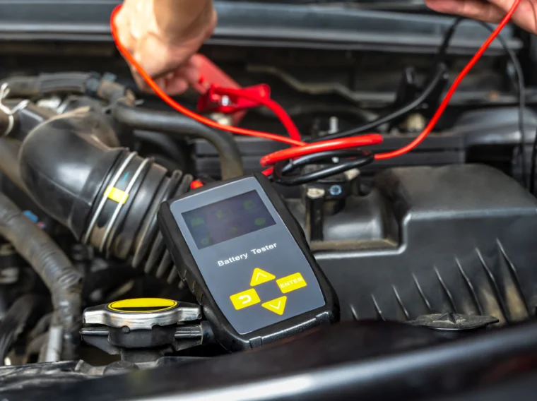 A mechanic using a car battery testing tool to check the battery of a vehicle.