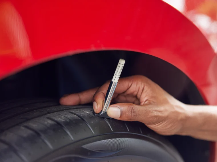 Close-up of an auto technician checking the tread of a tire with a gauge.