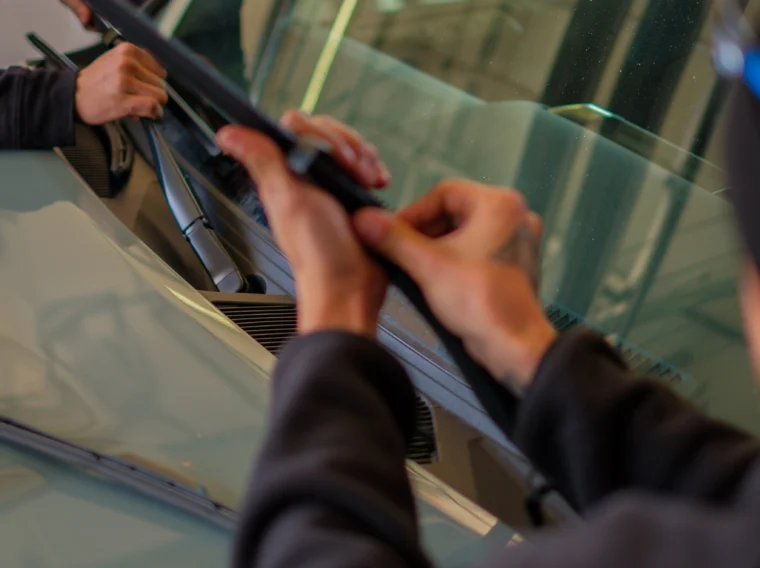 Two people are installing or replacing windshield wiper blades on a car as part of routine maintenance and State Inspection Services.